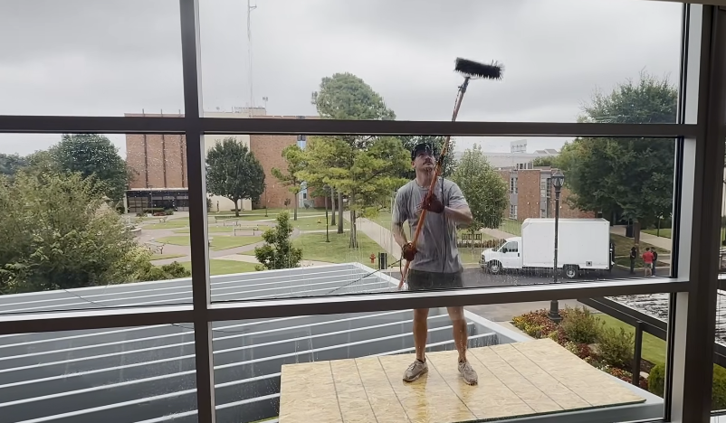 Window cleaning technician using a water-fed pole to clean large commercial glass windows