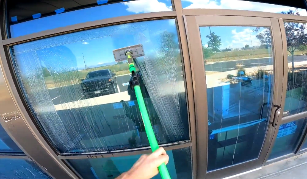 Commercial window cleaner using a green squeegee pole on a storefront glass entrance in San Clemente