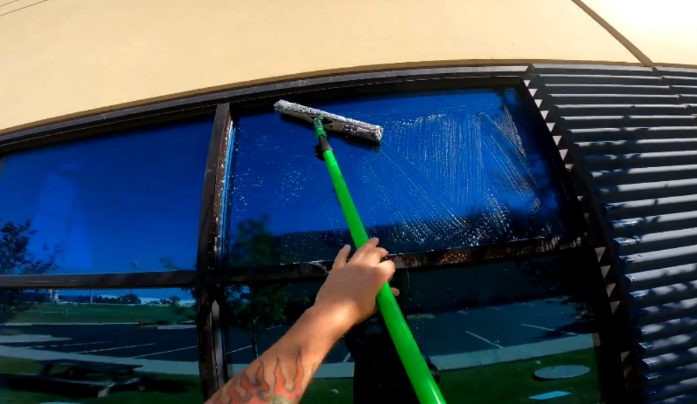Technician cleaning a tinted commercial window with an extension pole squeegee in San Clemente