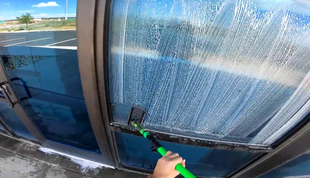 Commercial window cleaner working a squeegee pole across a large glass door panel in San Clemente