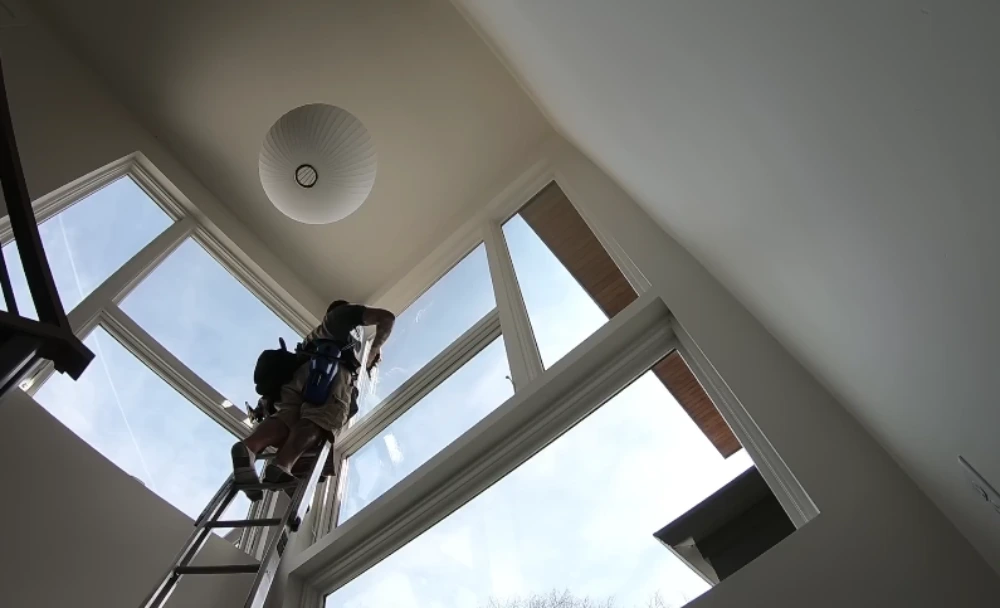 Technician on a ladder cleaning tall upper windows with a backpack water-fed system in San Clemente
