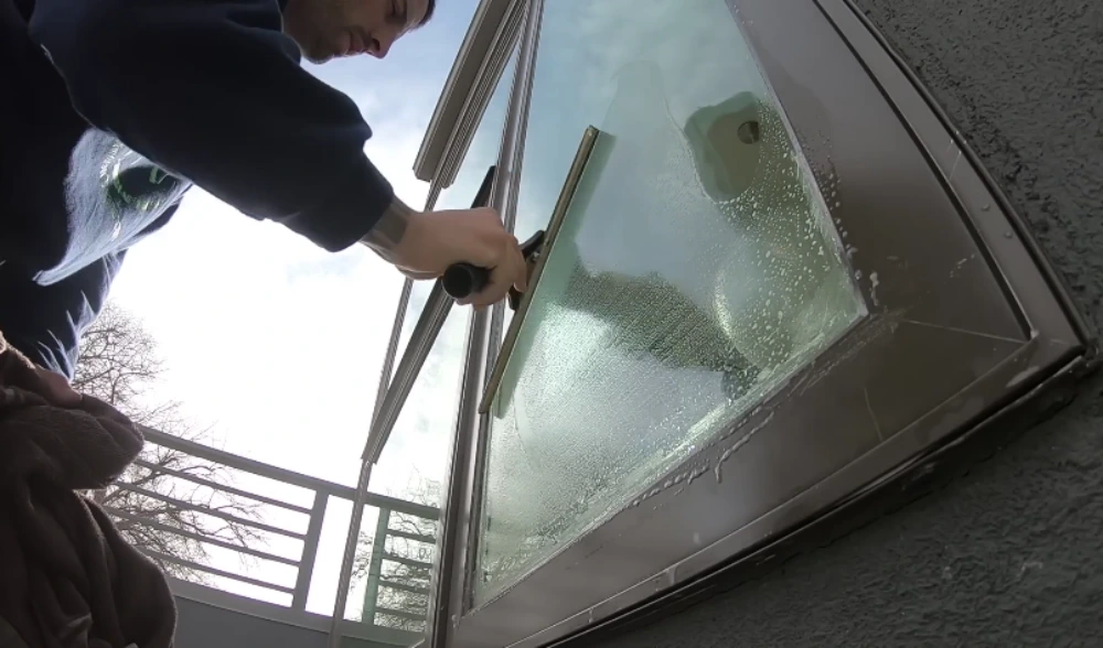 Technician squeegeeing an angled bay window from a balcony in San Clemente