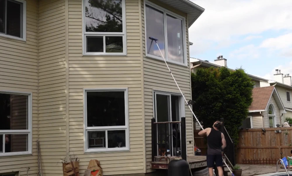 Window cleaning technician using a water-fed pole to clean second-story windows