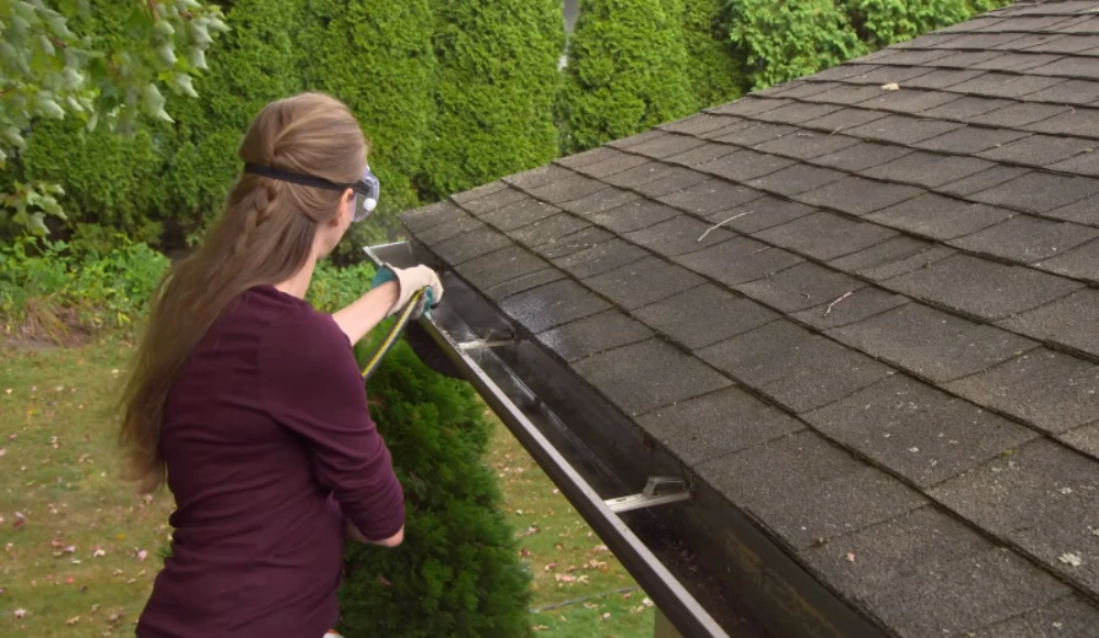 Technician cleaning debris from a roof gutter wearing safety goggles