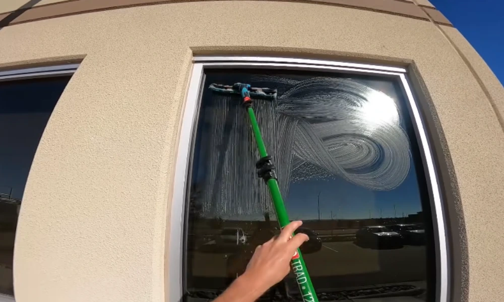 Technician using a squeegee pole to clean a large glass window pane in San Clemente