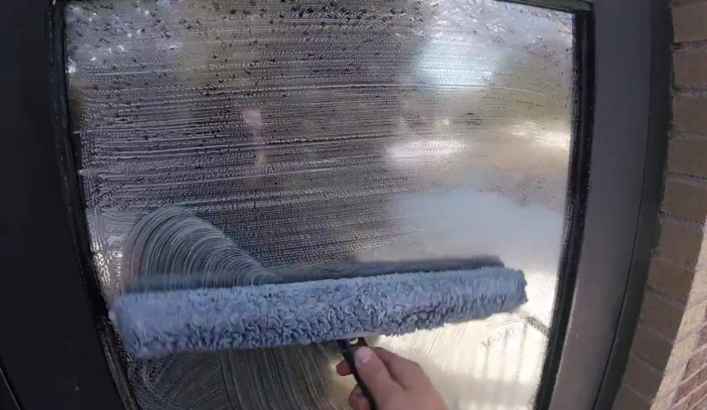 Close-up of a microfiber cleaning tool wiping streaks from interior window glass in San Clemente