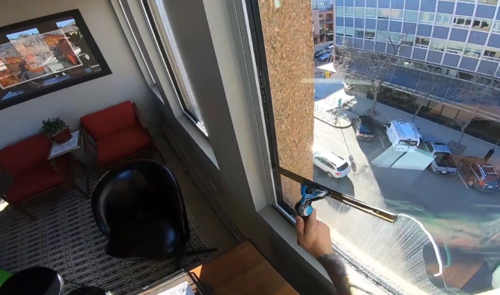 Technician cleaning a floor-to-ceiling office window overlooking the street in San Clemente