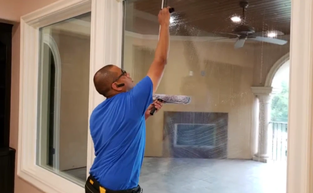 Window cleaning technician using an extension tool to clean a tall window in a luxury home