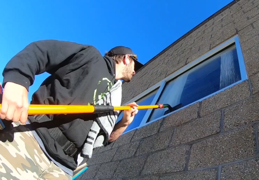 Window cleaning technician using a water-fed pole to reach upper-story windows from the ground