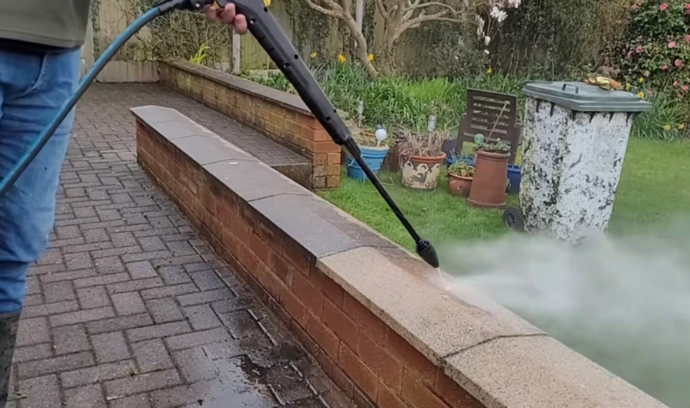 Technician pressure washing a brick garden wall and patio edge