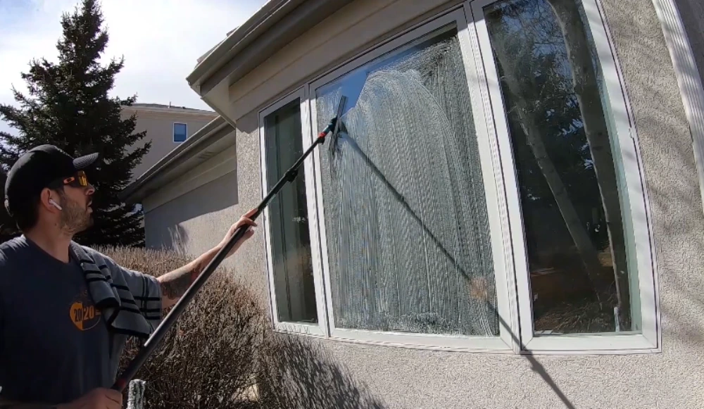 Professional window cleaner using a water-fed extension pole to clean a second-story window in San Clemente