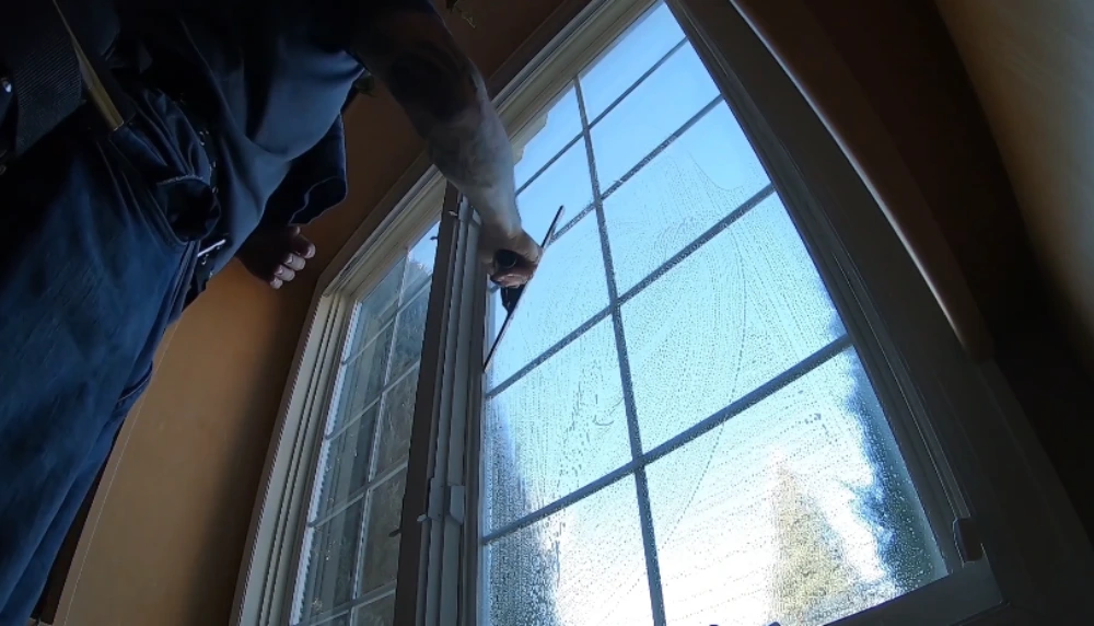 Interior window cleaning technician squeegeeing an arched window from inside a San Clemente home