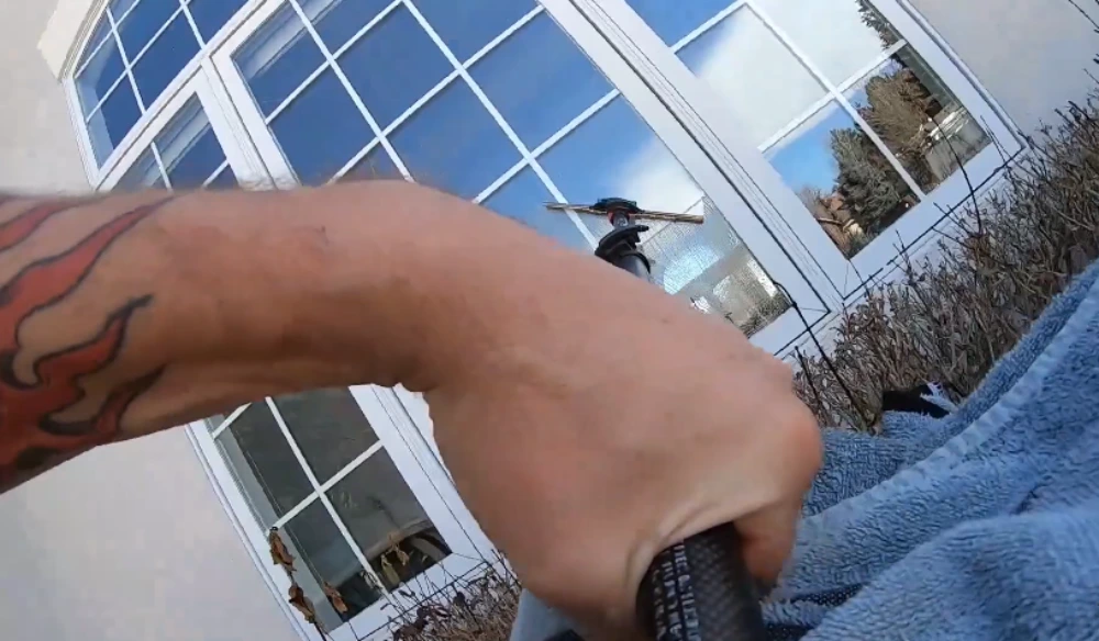 Technician's arm with towel beside a water-fed pole reflected in a clean San Clemente window