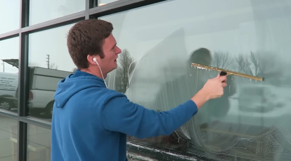 Commercial window cleaner using a traditional squeegee on large storefront glass in San Clemente