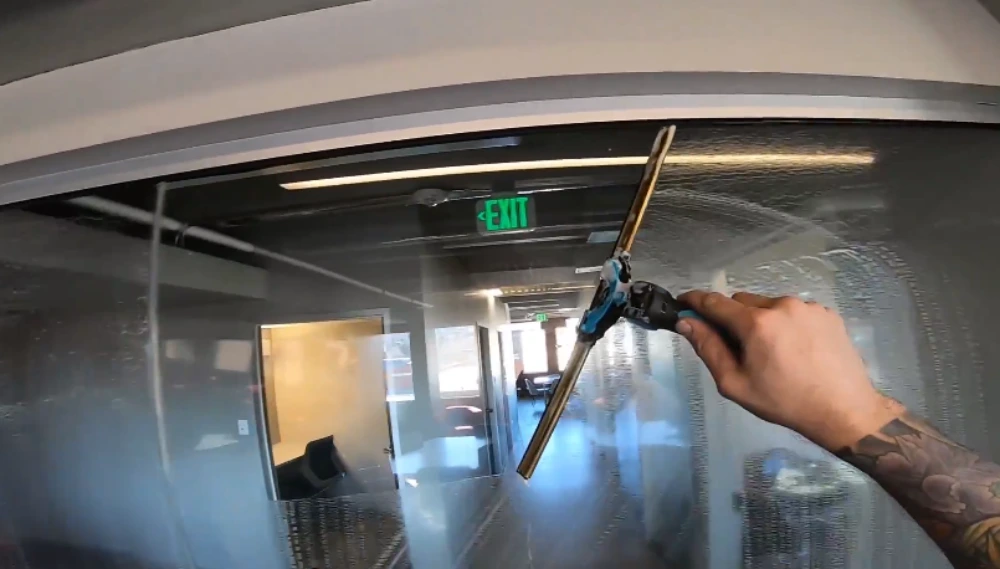 Close-up of a window cleaning technician using a squeegee on interior commercial glass
